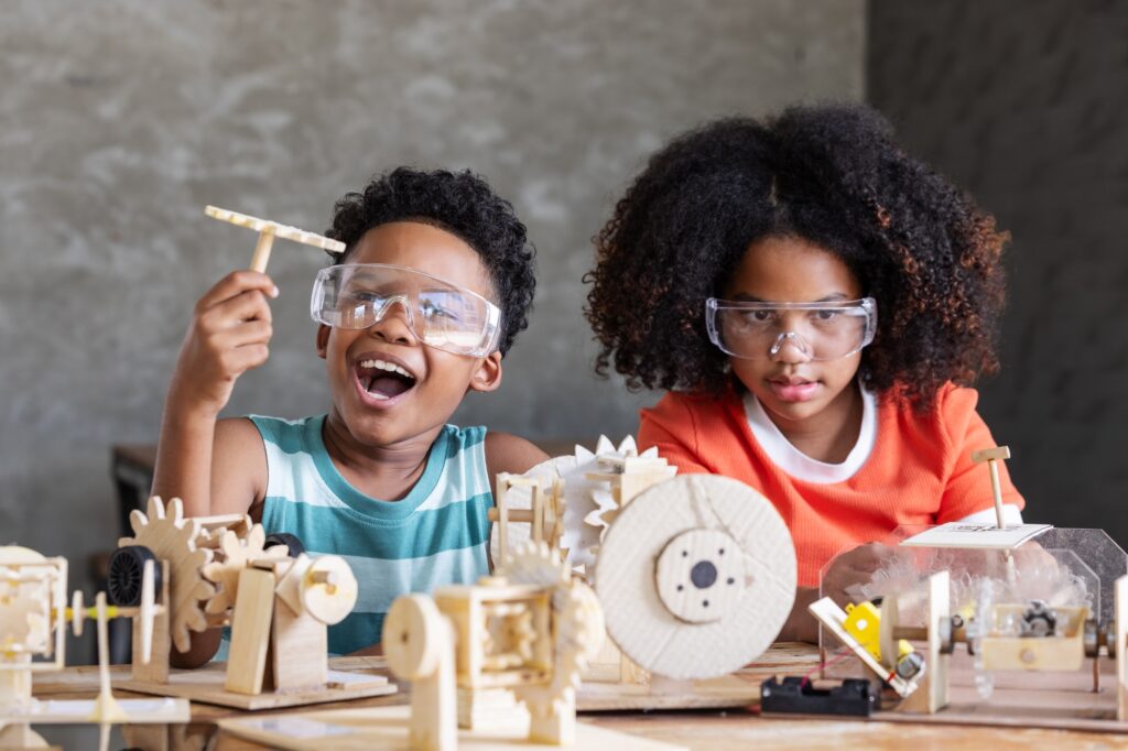 Two enthusiastic children wearing safety goggles are engaged in a STEM project